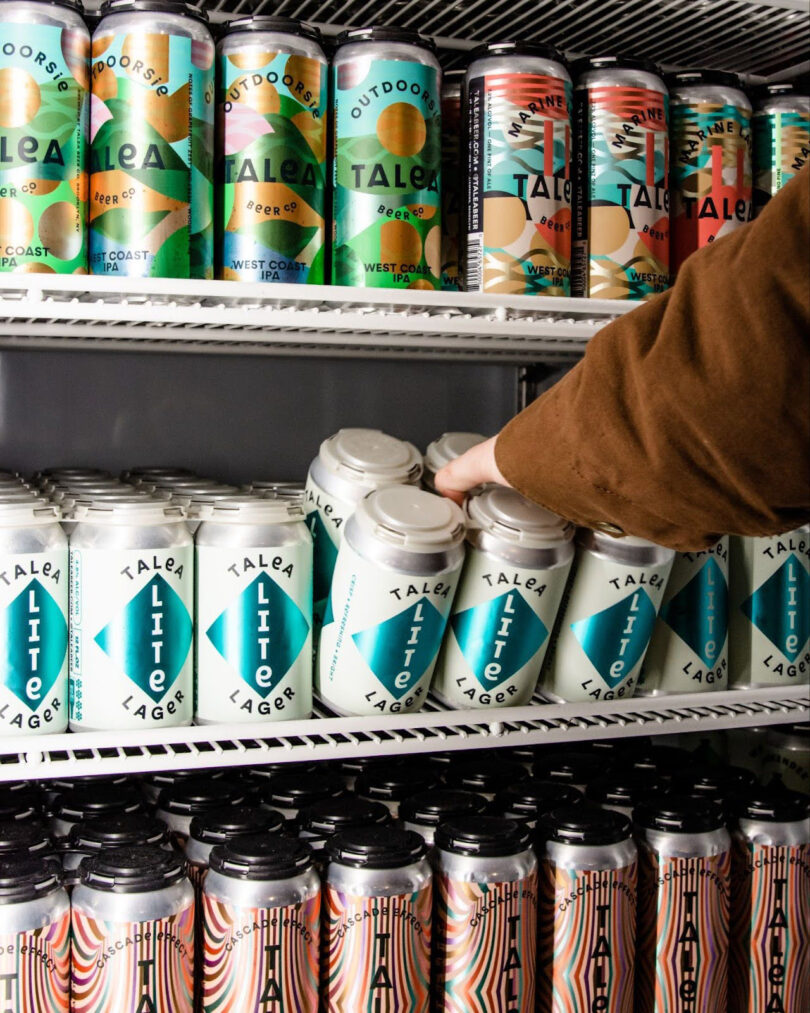 A person picking up cans of beer in a refrigerator.