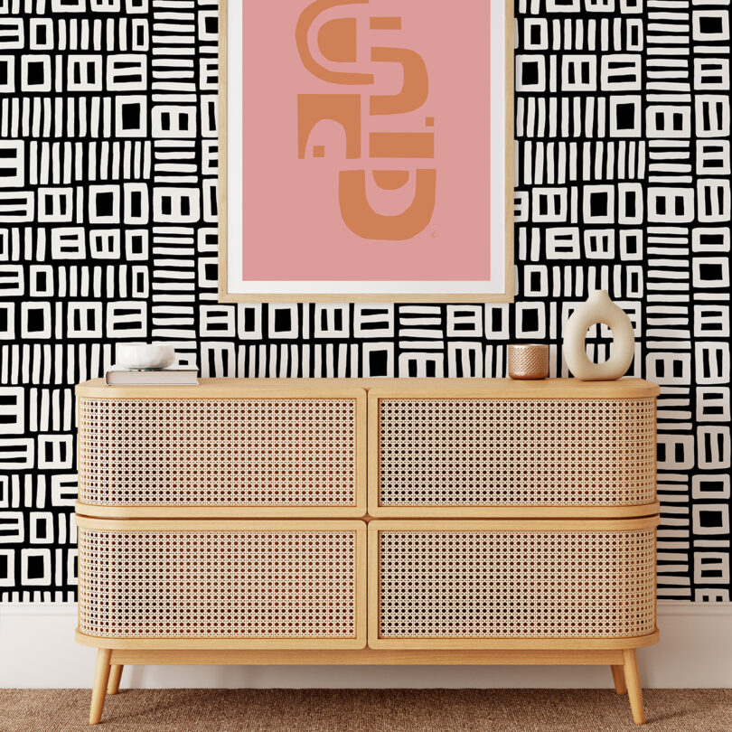 light wood credenza sits in front of a wall covered in black and white patterned wall paper