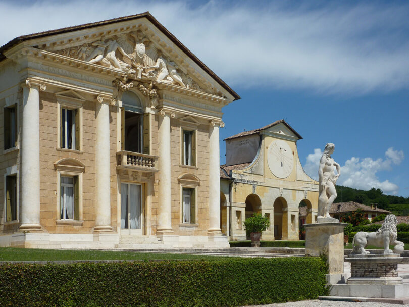 Classical villa with a statue in the foreground and clear blue skies.