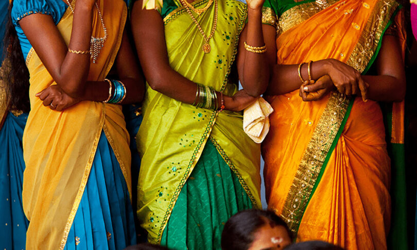 Three women in colorful sarees standing together.