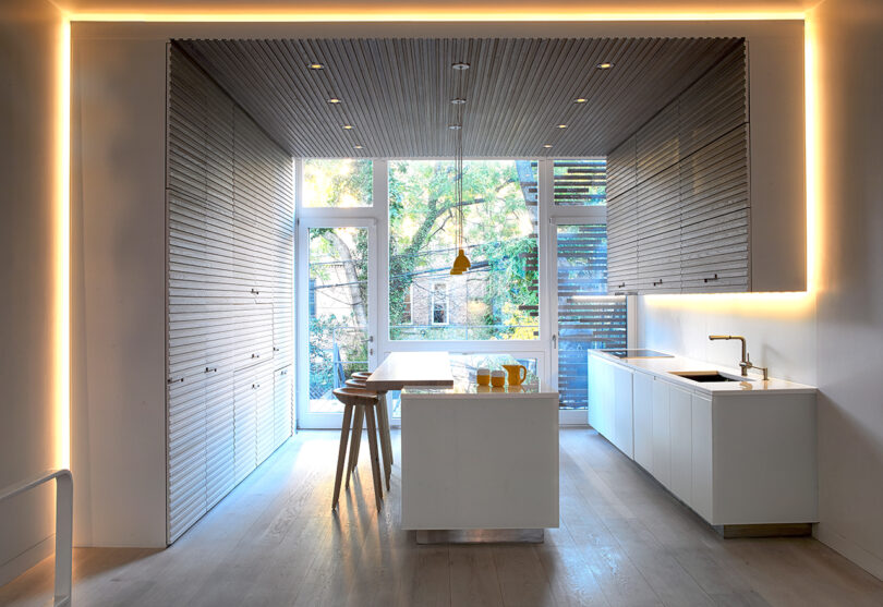 Modern kitchen with minimalistic design, featuring clean lines, under-cabinet lighting, and large windows.