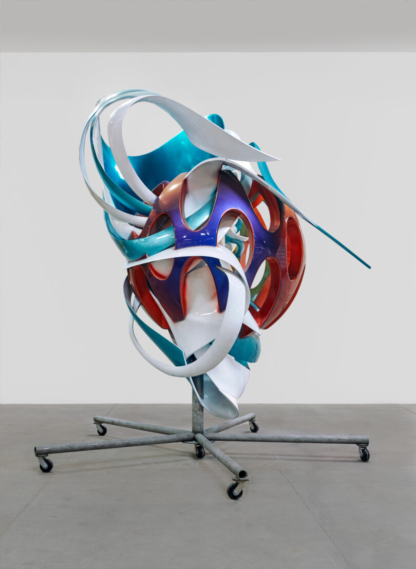 Abstract swirling sculpture on a wheeled metal base.