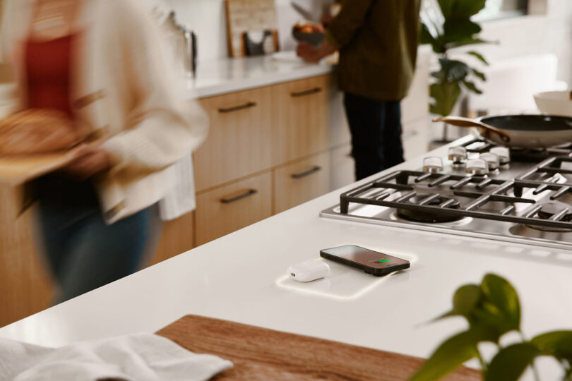 A woman is preparing food in a kitchen with a wireless charging station nearby to a gas cooktop.
