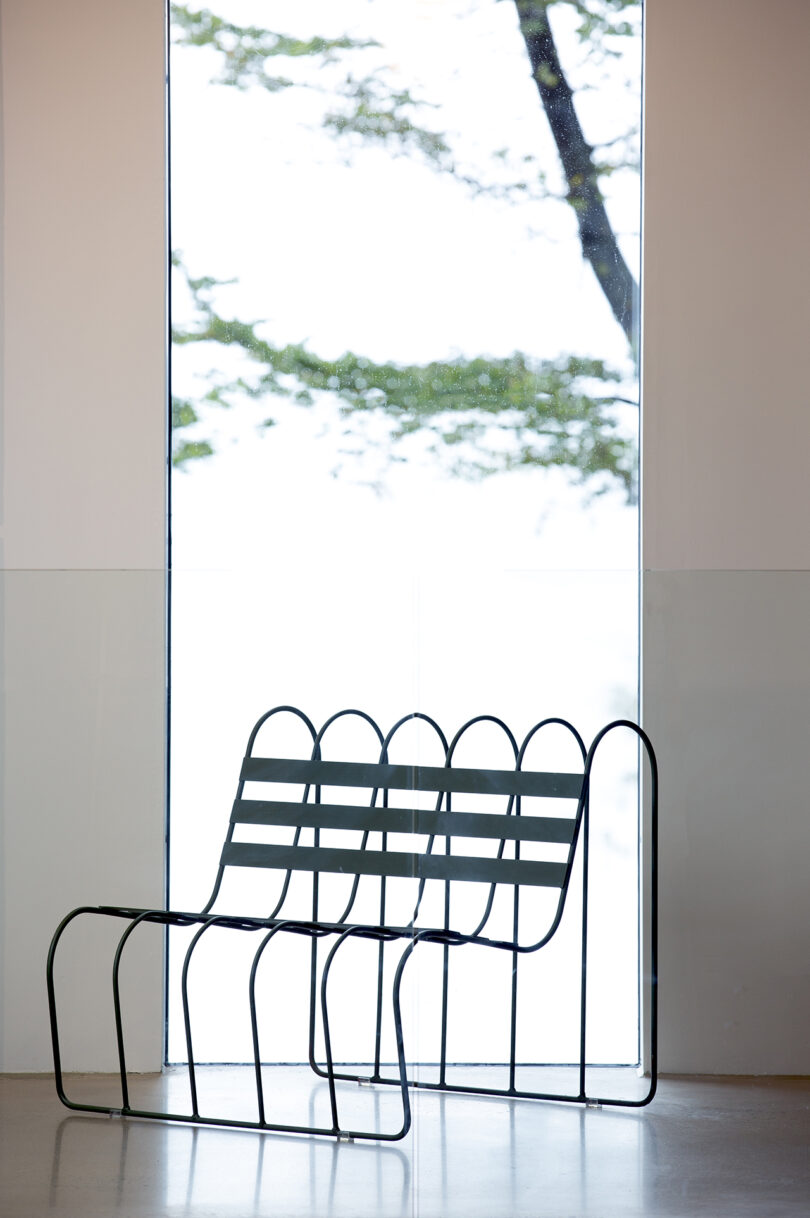 A minimalist metal bench situated in a bright room with a large window.