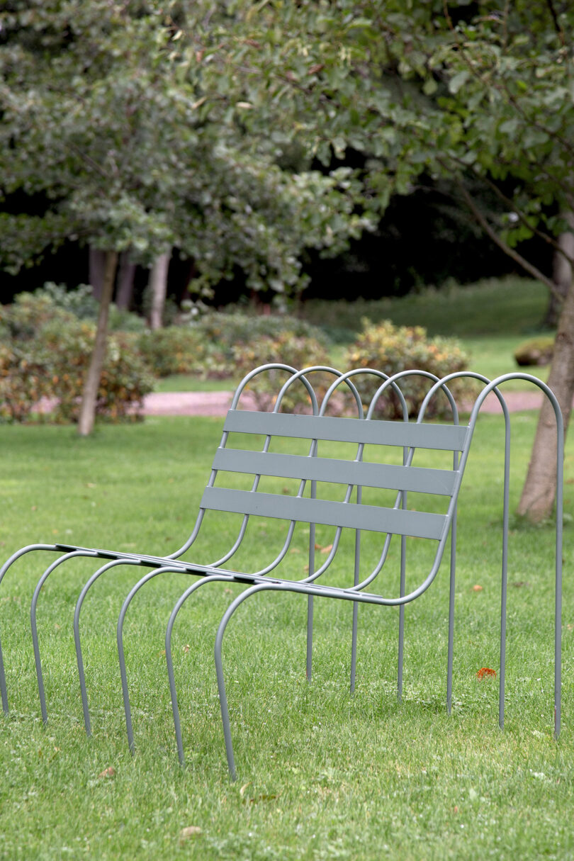 A minimalist metal bench outdoors in the grass.