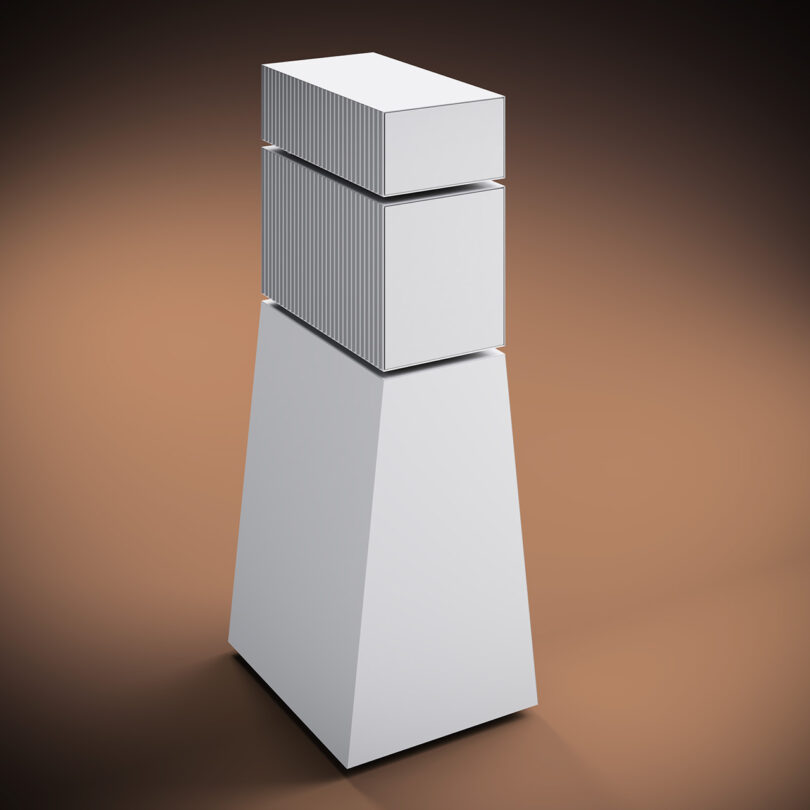 Goldmund Theia wireless speakers resembling a silver geometric sculpture consisting of a cylinder and two cubes on a pedestal against a gradient background.