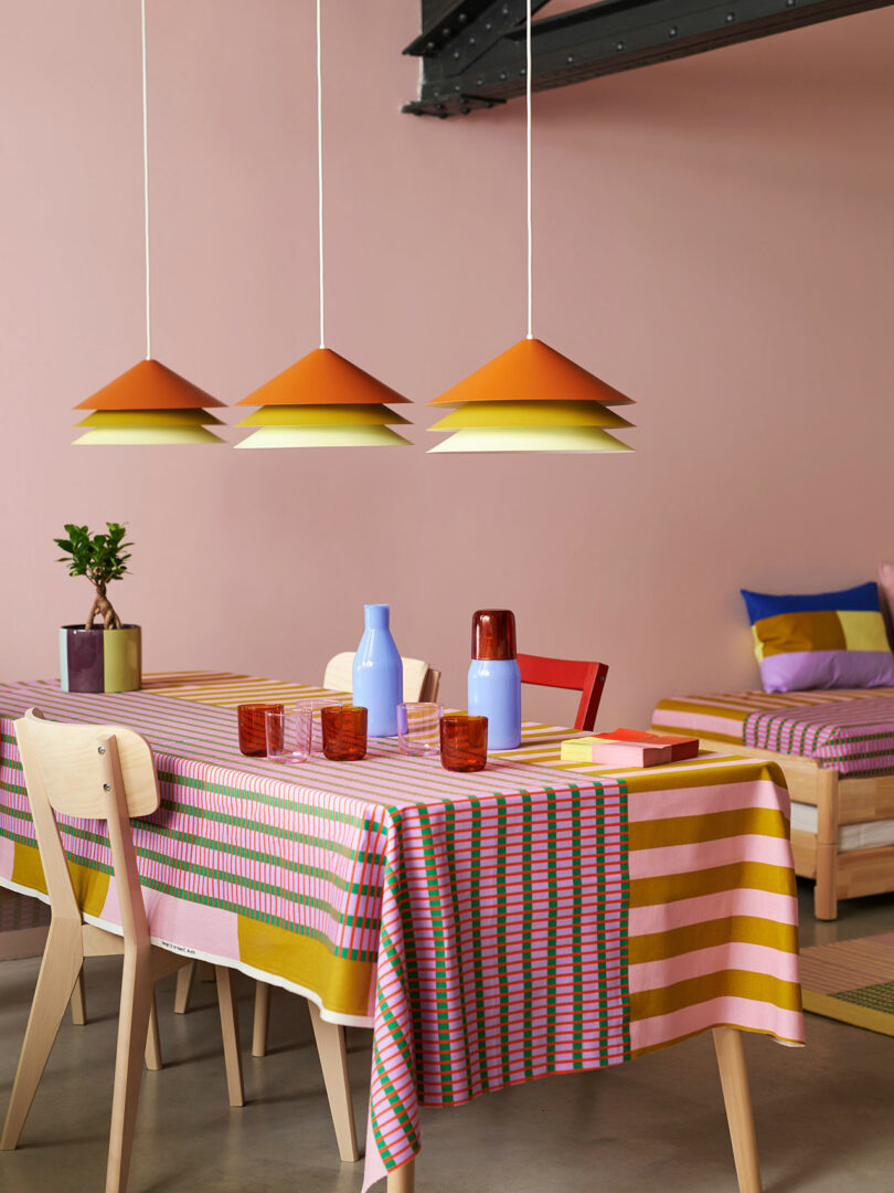 angled view of modern dining table with colorful patterned tablecloth, layered pendant lighting, and colorful glasses