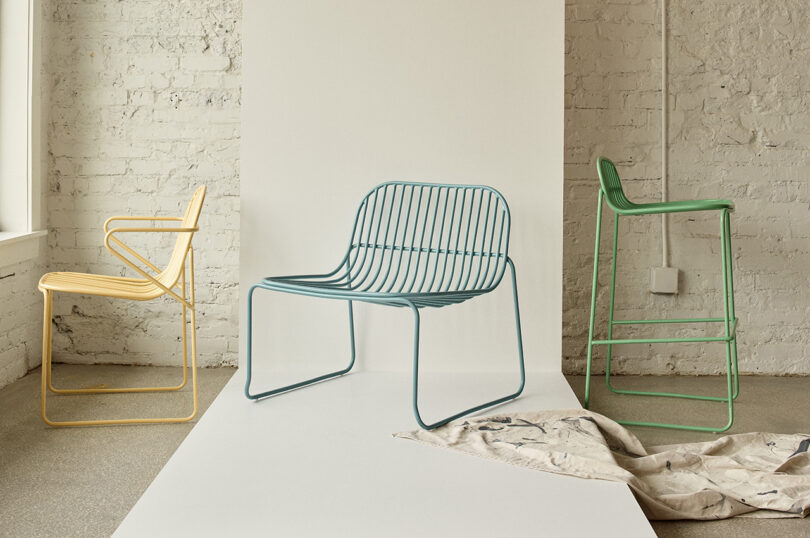 Três cadeiras contemporâneas coloridas com design minimalista em uma sala iluminada com paredes de tijolos brancos.