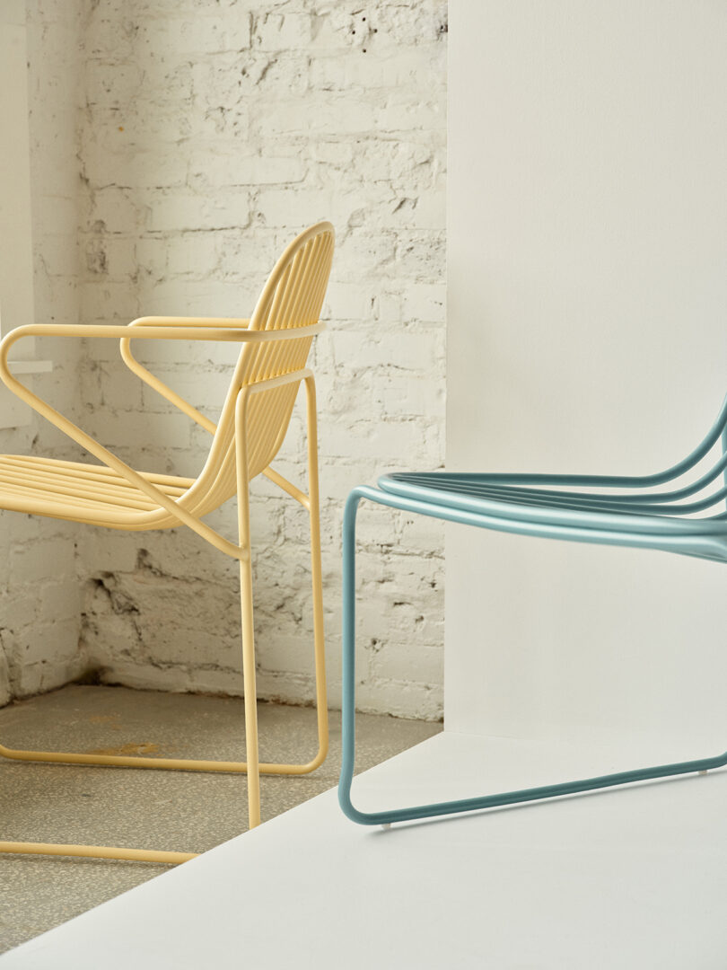 Duas cadeiras contemporâneas coloridas com design minimalista em uma sala iluminada com paredes de tijolos brancos.