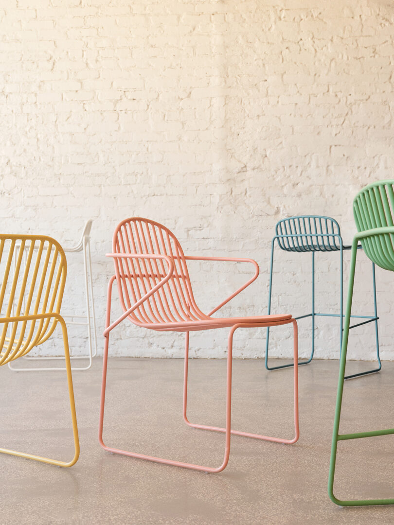 Quatro cadeiras contemporâneas coloridas com design minimalista em uma sala iluminada com paredes de tijolos brancos.