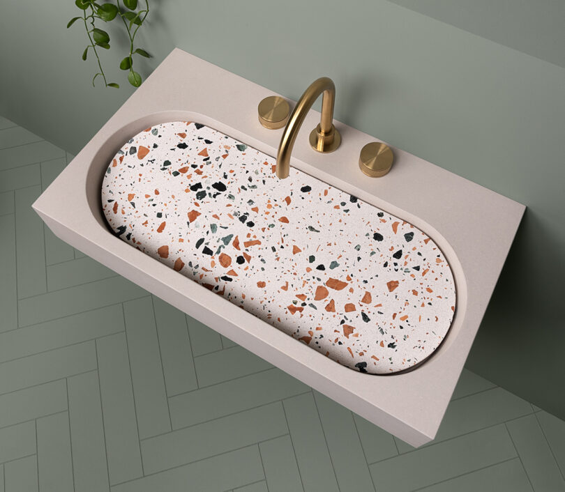 A sink with a concrete surface with terrazzo insert in a light green bathroom with tile zig-zag flooring