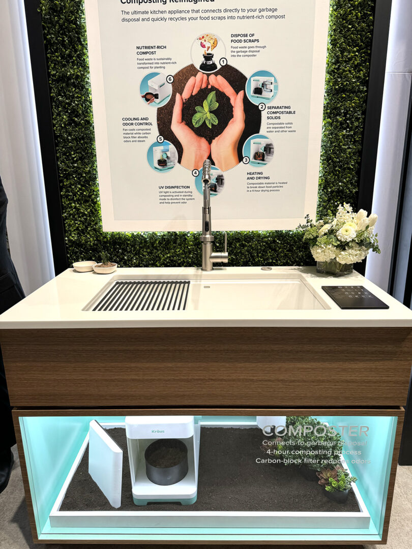 A kitchen sink featuring a see-through basin display revealing a compost system concept beneath. A large sign with a hand cupping soil and a small plant above the sink explains the circular composting process in 6 different steps.