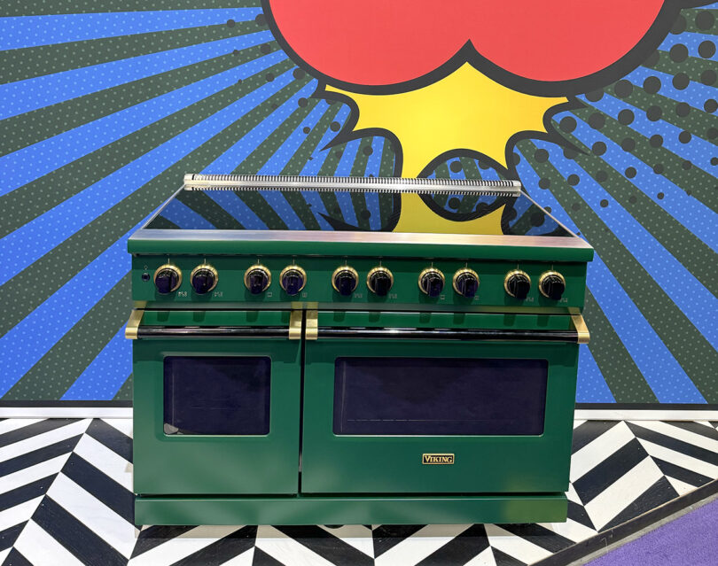 A green induction 48" stove with black knobs displayed at KBIS against a pop art styled background and graphic black and white floor