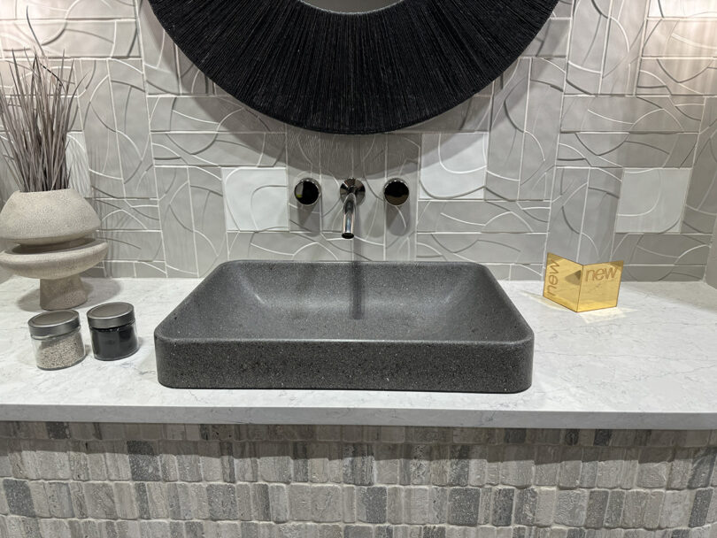 A bathroom with a circular mirror and wall mounted fixtures above a recycled material manufactured sink with dark grey terrazzo finish.