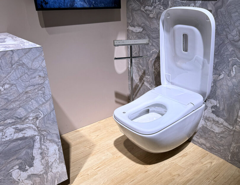 A wall mounted TOTO toilet in a bathroom featured at KBIS, staged attached to a marbled wall.
