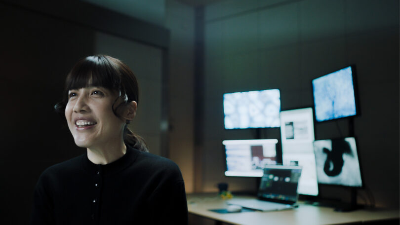 Digital artist Kaoru Tanaka in her studio smiling seated in front of her five external monitors and laptop