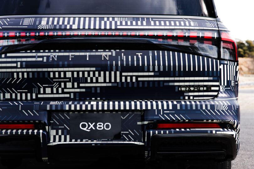 Rear right corner section of the new Infiniti GX80 wrapped in a monochromatic dash and square pattern designed by digital artist Kaoru Tanaka with "QX80" license cover.
