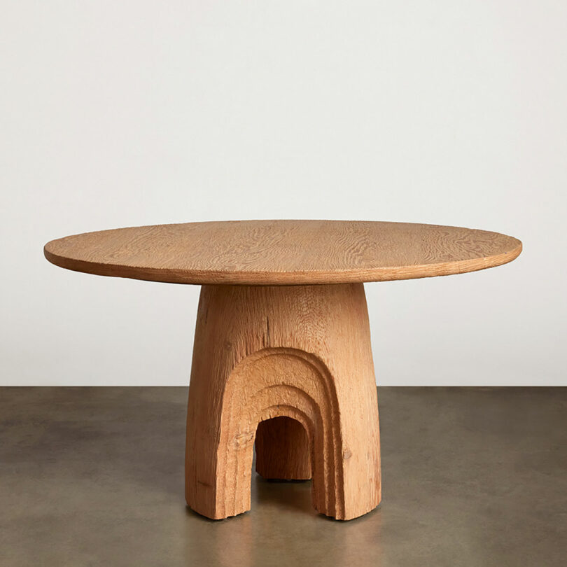 Round wooden table with a central column support featuring an arch-shaped cutout.