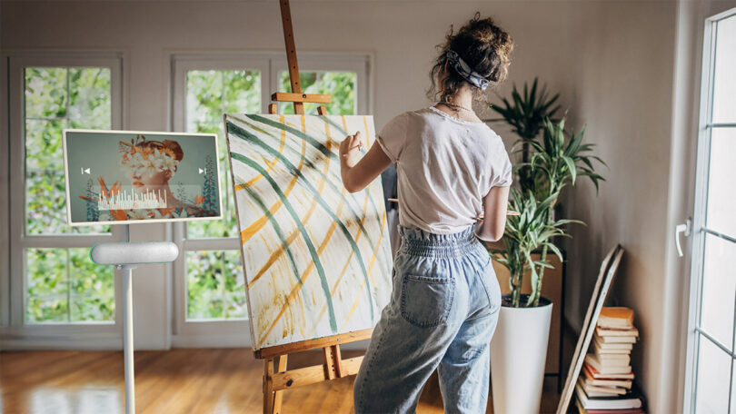 An artist painting on a canvas in a bright, home studio, accompanied by music from an LG StanbyME Speaker and Rollable Display