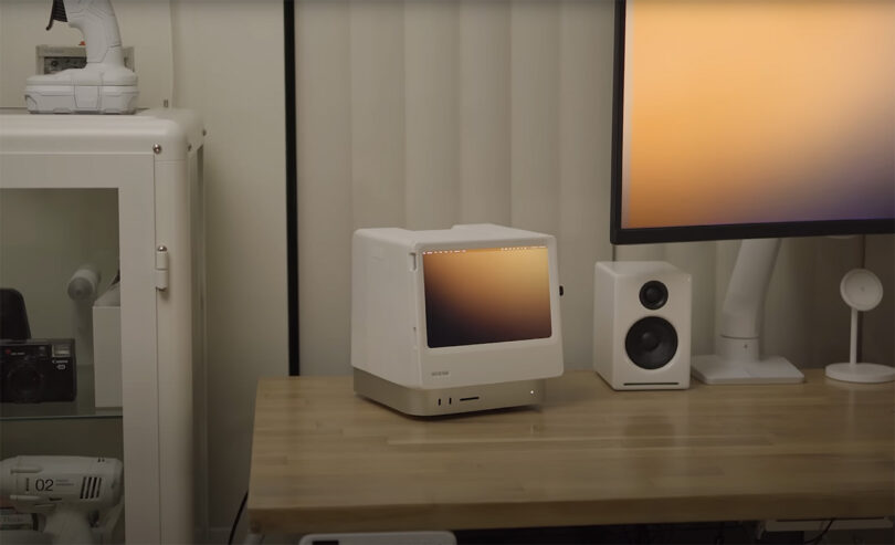 A 3D printed Macintosh Studio dock sits on a desk beside modern speakers and a widescreen monitor