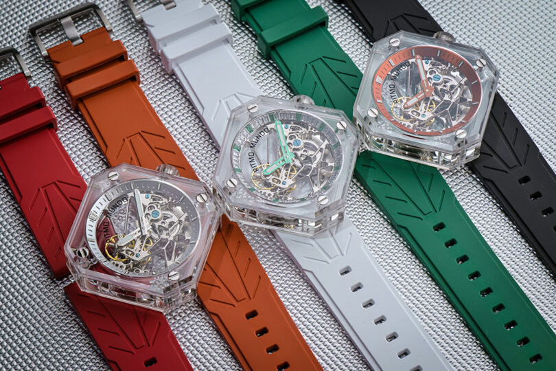 A collection of three Ritmo Mundo Pegasus watches cases set separately over a selection of red, orange, white, green and black straps, displayed side by side.