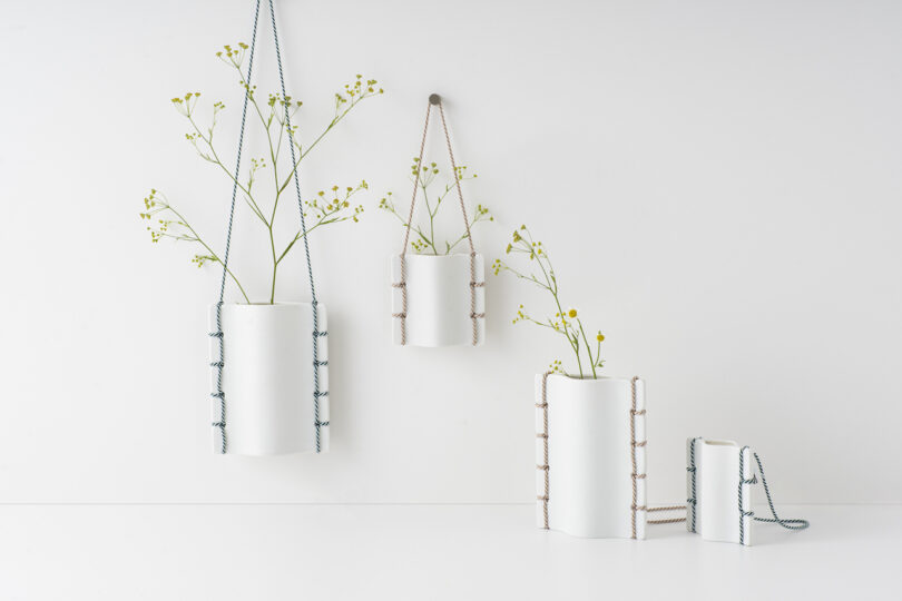 four white ceramic vases with simple foliage hanging on a white wall and on a white table