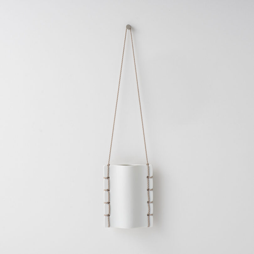 ceramic vase hanging on a white wall by a thread