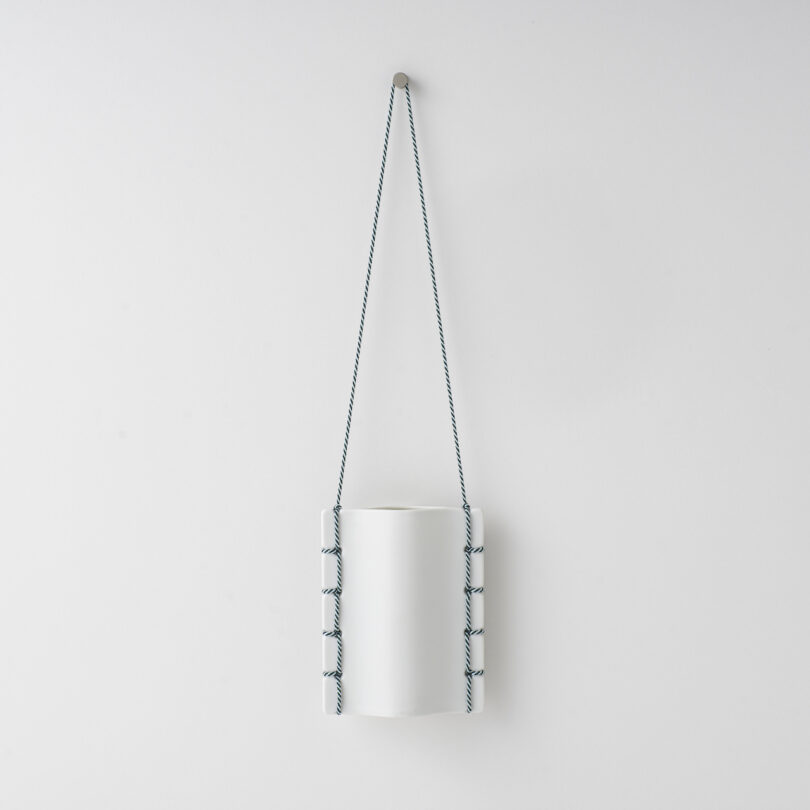 ceramic vase hanging on a white wall by a thread