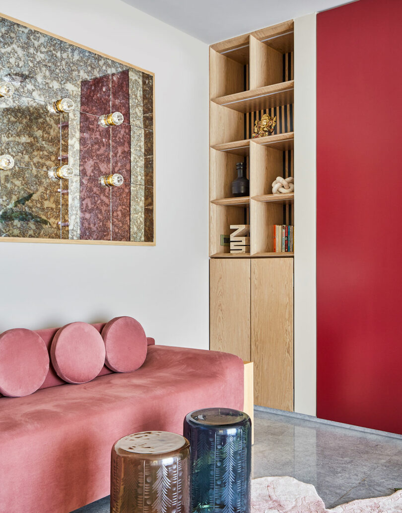 فضای استراحت مدرن با مبل مخملی صورتی، یک قفسه کتاب چوبی، و پانل دیواری مرمری پرآذین.