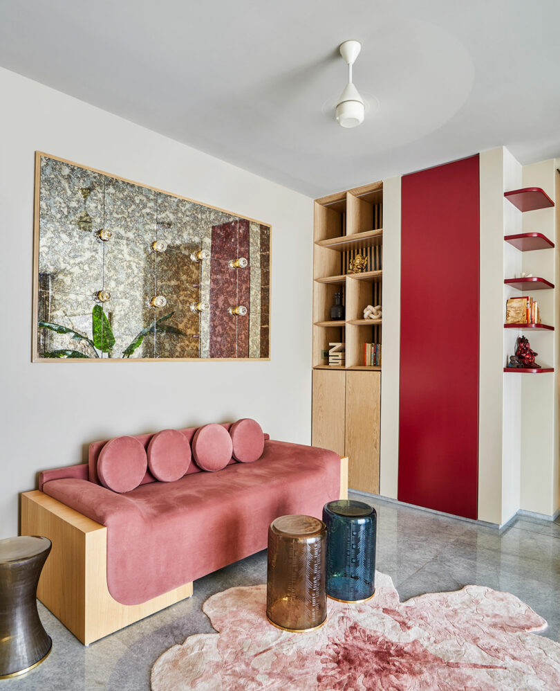 A modern lounge space featuring a pink velvet sofa, a wooden bookshelf, and an ornate marbled wall panel.