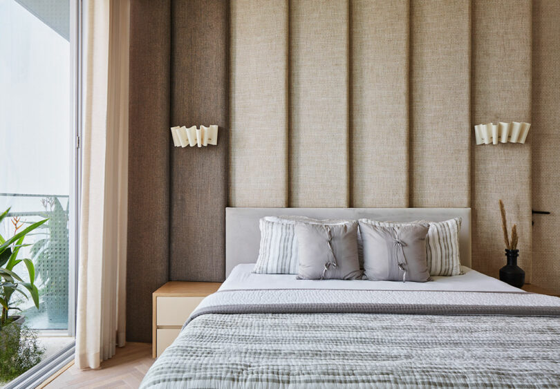 Modern bedroom interior with neutral tones featuring a padded wall panel, and contemporary lighting.