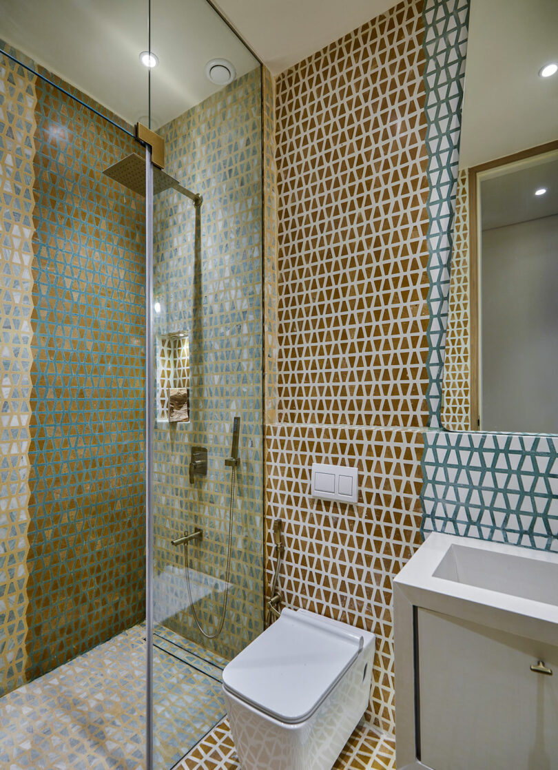 Modern bathroom featuring colorful patterned tiles, glass shower enclosure, and white fixtures.