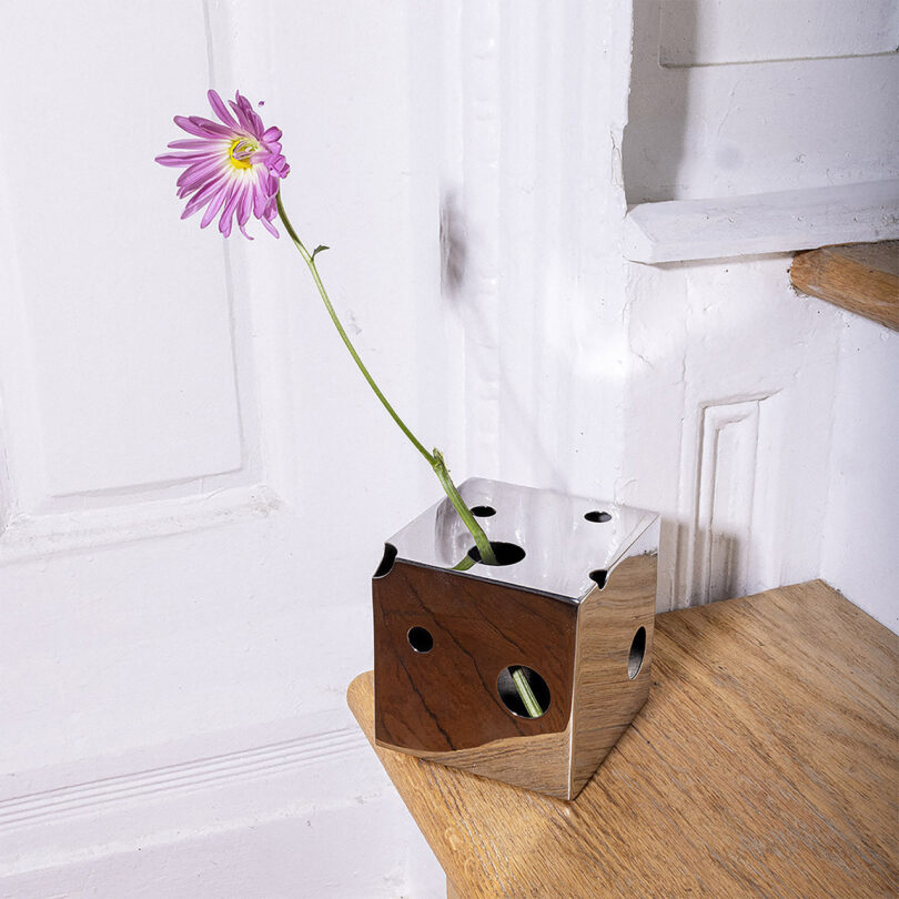 A mirrored cube-shaped vase with a flower in it.