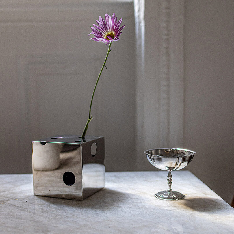 A mirrored cube-shaped vase with a flower in it and a silver coupe.