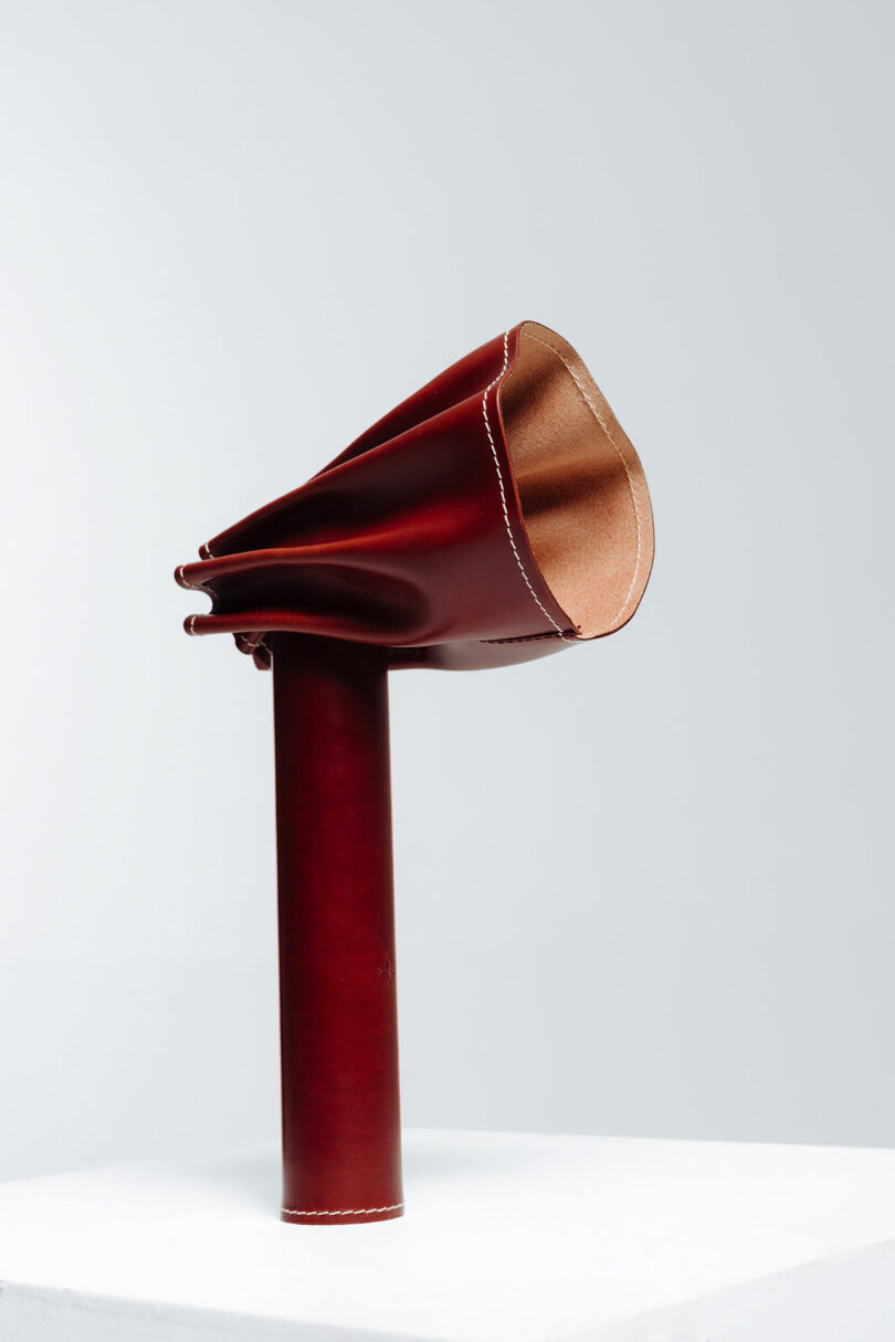 A red leather lamp standing upright on a white surface against a light grey background.