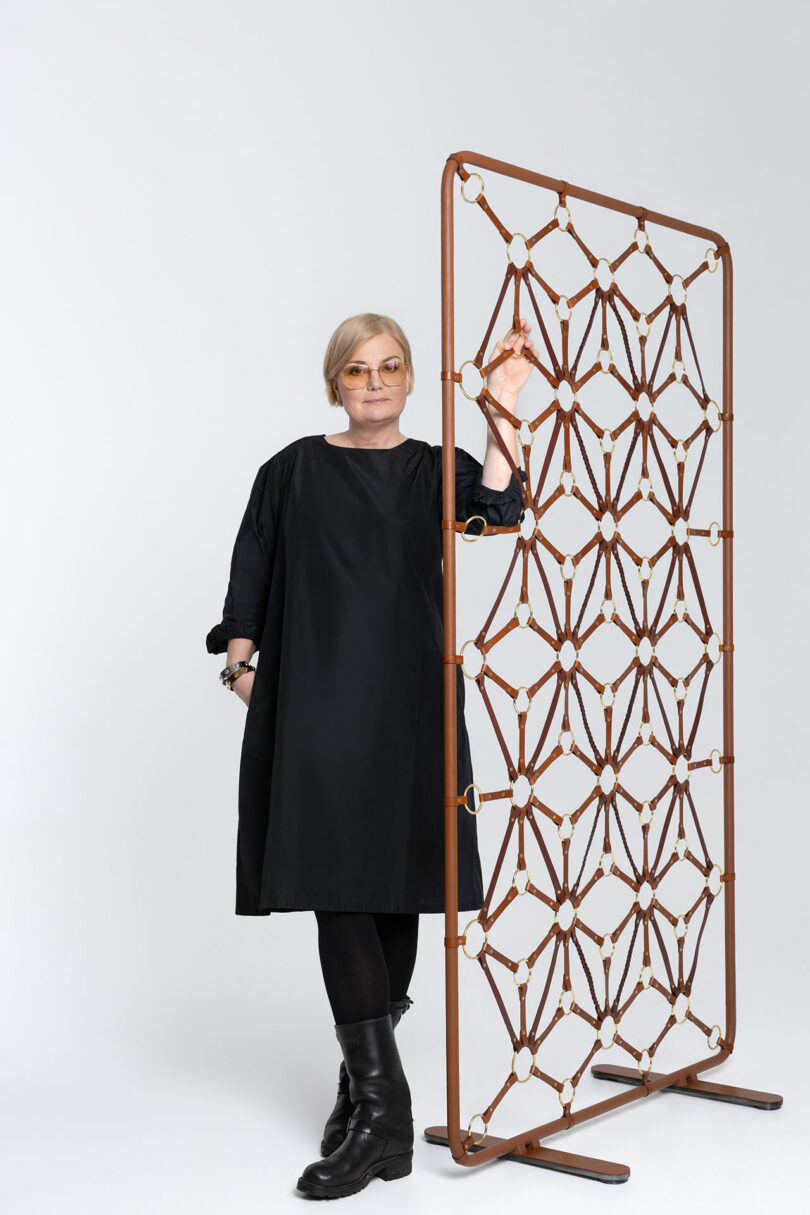 Woman in a black dress standing beside a geometric leather screen.