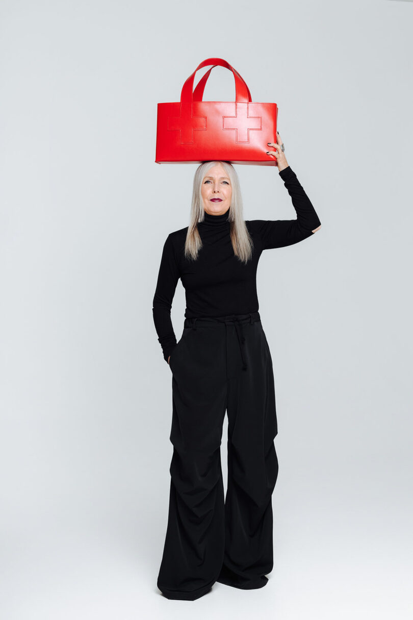 A woman in a black outfit holds a large red tote bag above her head.