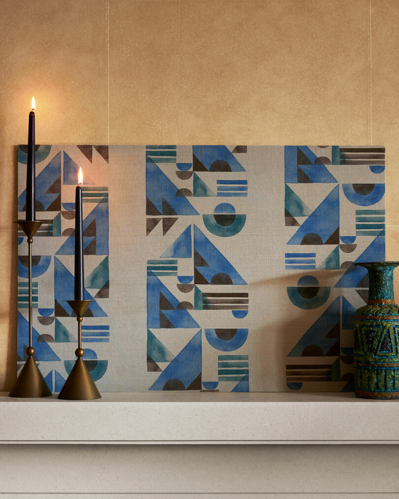 Contemporary geometric artwork displayed on a mantel with a lit candle and decorative objects.