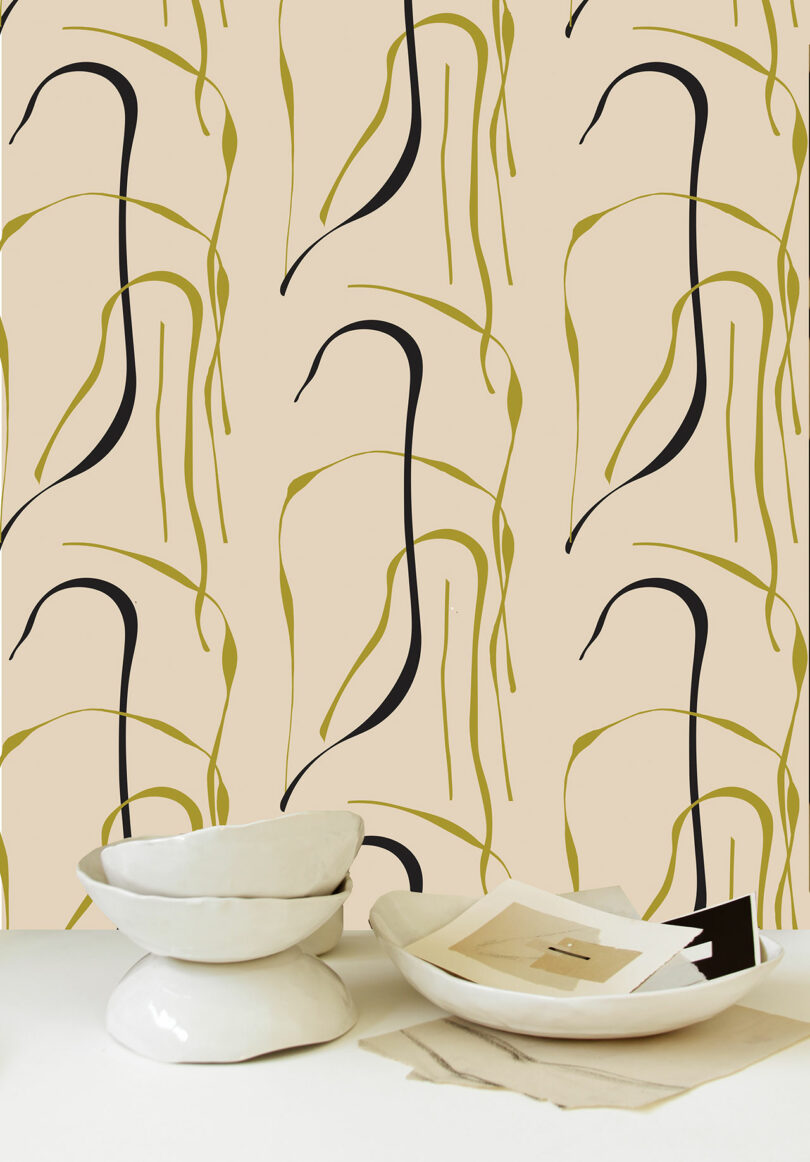 Abstract patterned wallpaper with organic shapes in black and green, with a marble bowl and plate containing paper cutouts in the foreground.