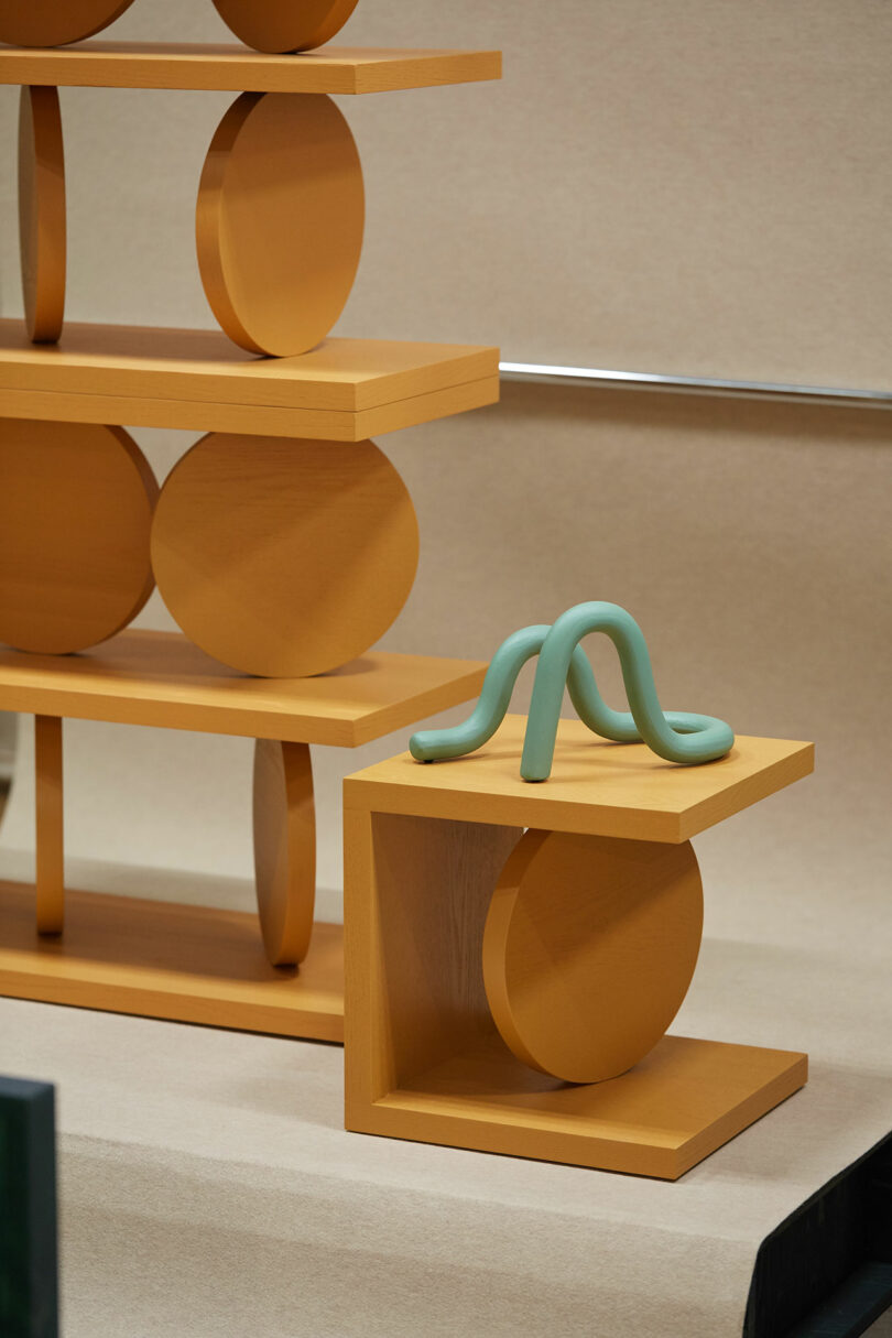 A modern wooden shelving unit with circular elements and a sculptural aqua-colored object on one of its shelves.
