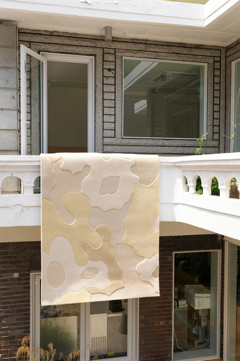A modern rug with puzzle piece designs hangs over a balcony in an urban setting.