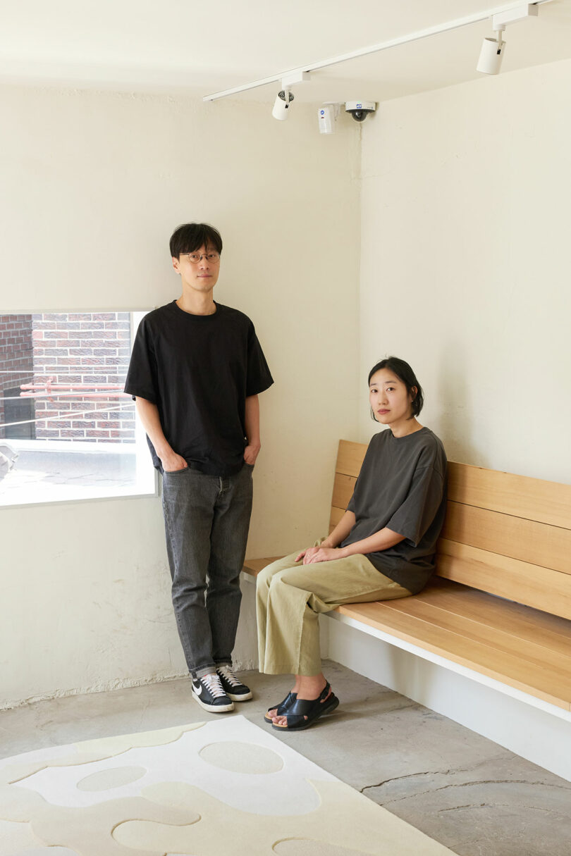 Two individuals in a room with a wooden bench by the window.