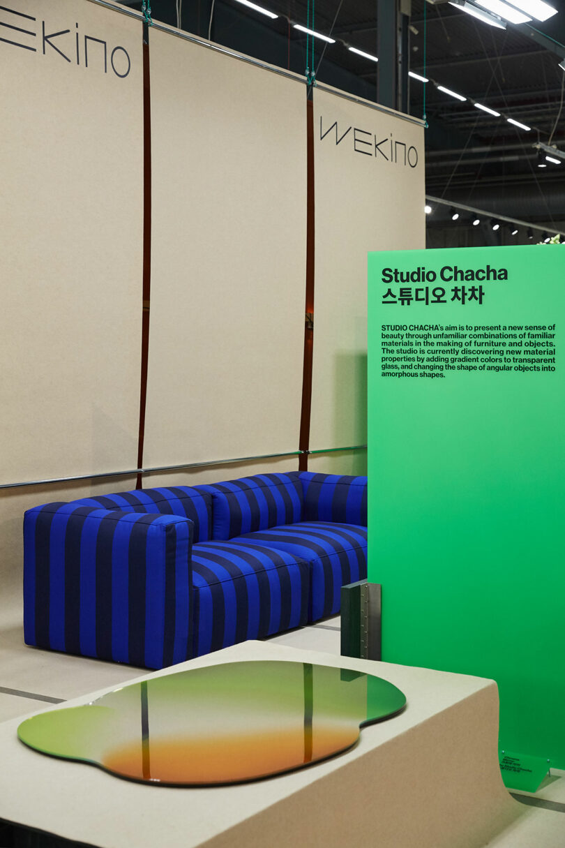 Modern exhibition space with a green backdrop, minimalist furniture, Wekino informational wall text.