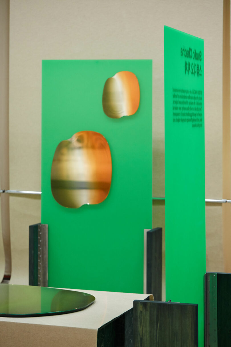 Abstract mirror installation featuring green panels with circular cutouts and metallic spheres.
