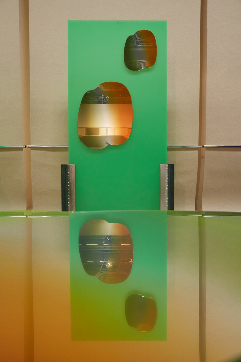 Green rectangular panel with circular cutouts, reflected on a glossy surface.