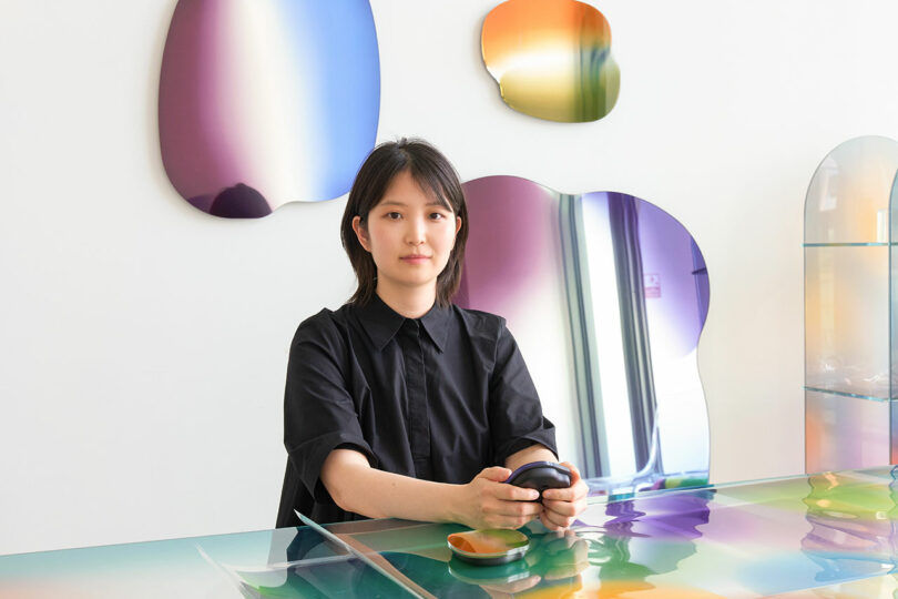 Woman in a black shirt sitting at a colorful, reflective Wekino table in a modern space.