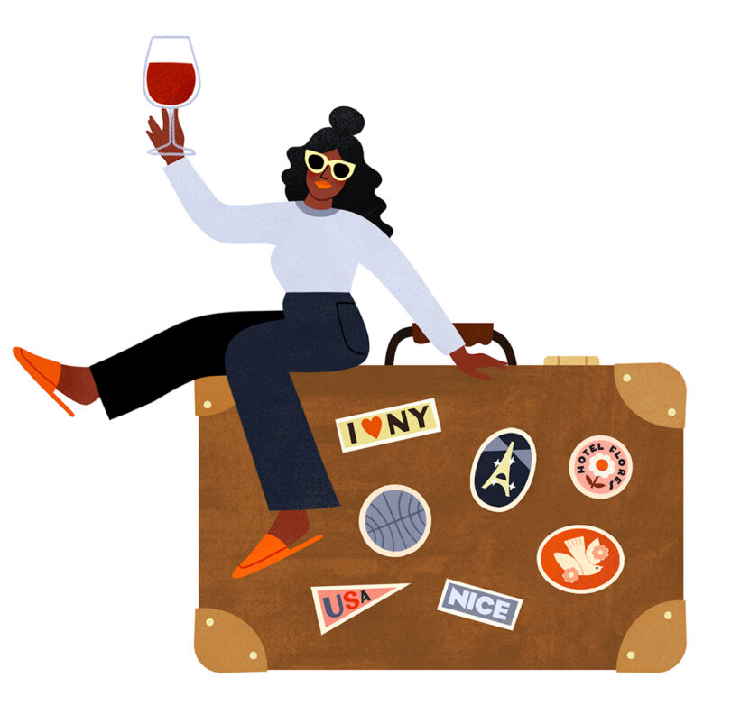 Woman sitting on a suitcase holding a glass of wine, with travel stickers on the luggage.