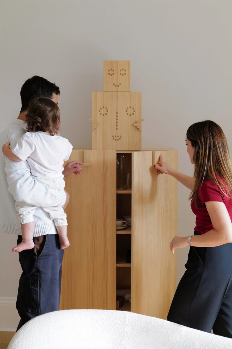 man, woman, and baby next to a wooden cabinet