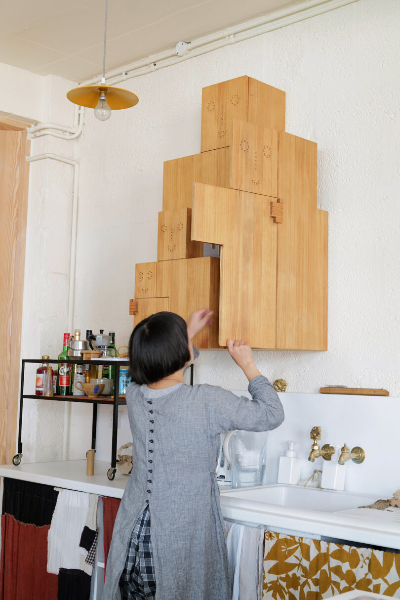 Woman arranging opening wooden cabinet on a white wall.