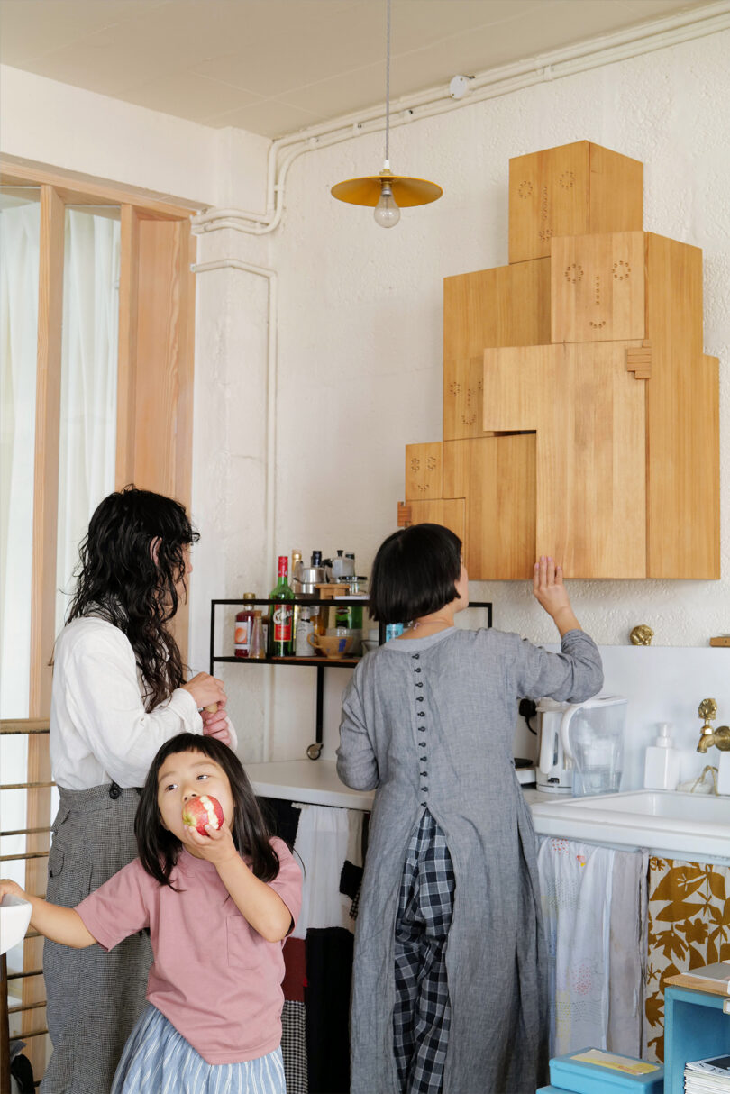 two woman and child standing in a kitchen next to a wooden cabinet